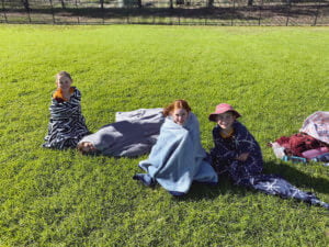 Students were freezing in the cold weather. They kept warm by snuggling up with a blanket while on the sidelines.